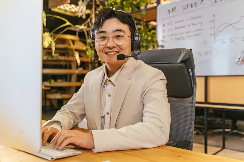 a man sitting at a desk on his laptop while wearing a headset