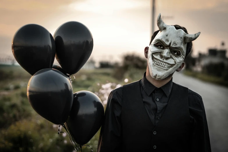 a man with a white skull face and black balloons