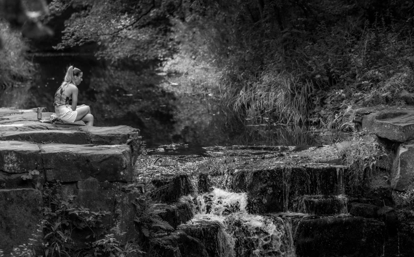 black and white image of a woman in a bathing suit sitting on a rock near waterfall