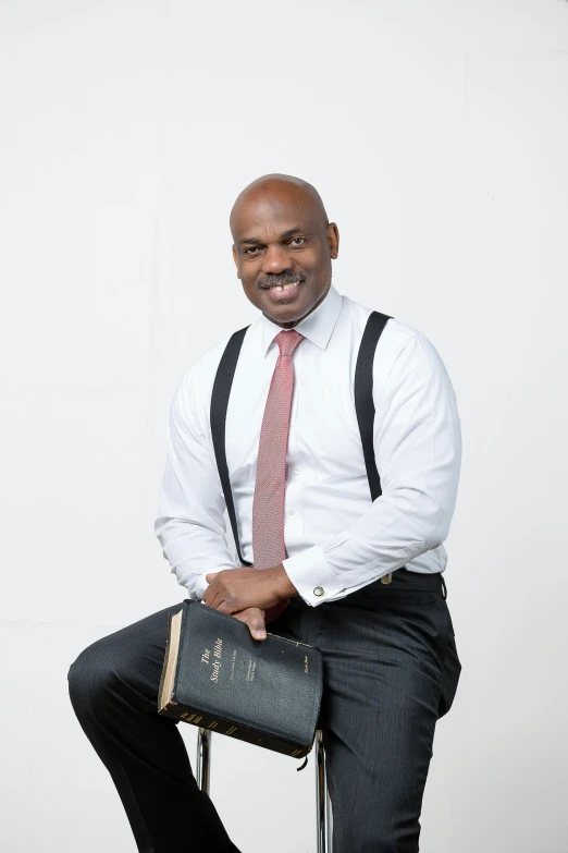 a man in white shirt and tie sitting on stool with legs crossed