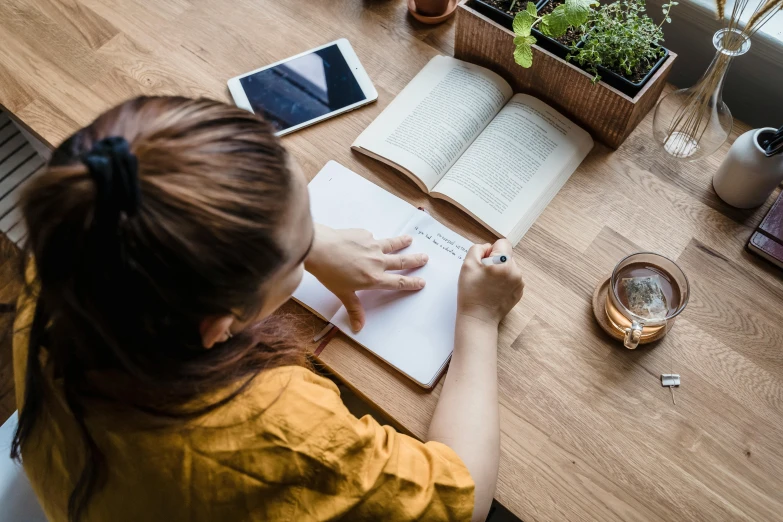 a woman doing a recipe on her note book with greenery on the table