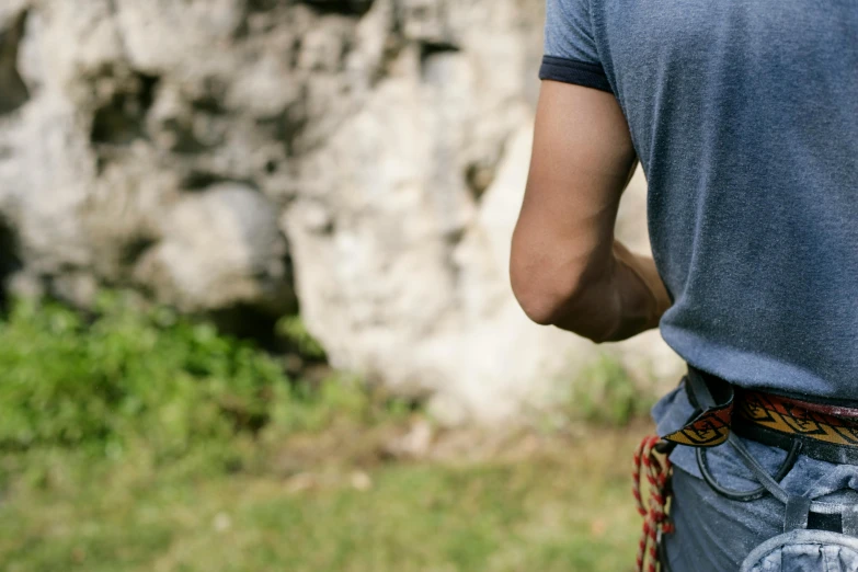 a man with a belt on standing next to a big rock