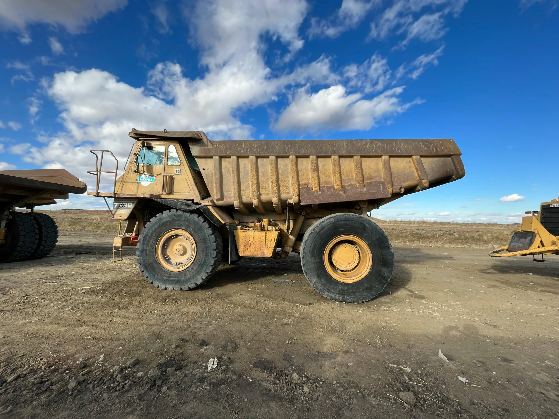 two large brown dump trucks in a dirt field