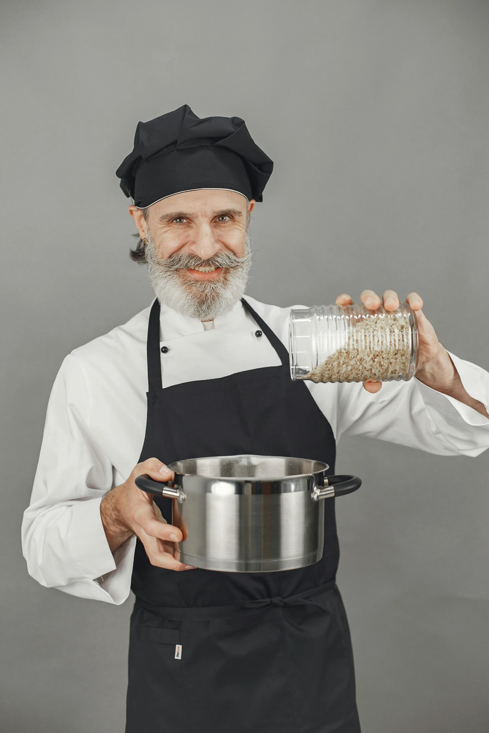 a man in a chef's uniform and hat, pouring some grains into a pan