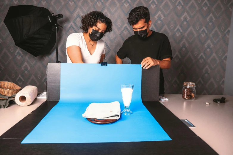 two people sitting at a table, the one on the top of a blue backdrop