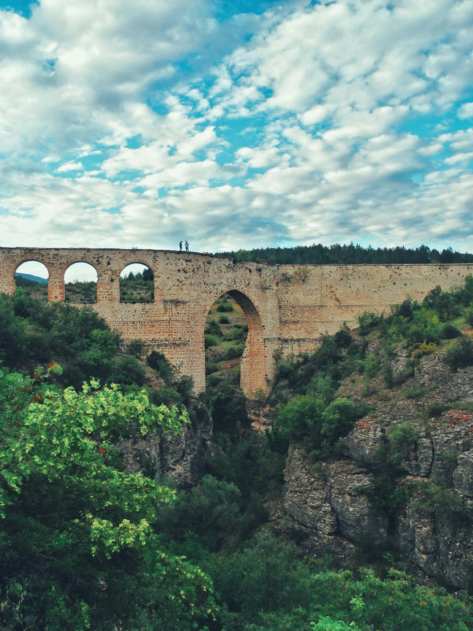 a man riding on the back of a horse in front of a stone bridge