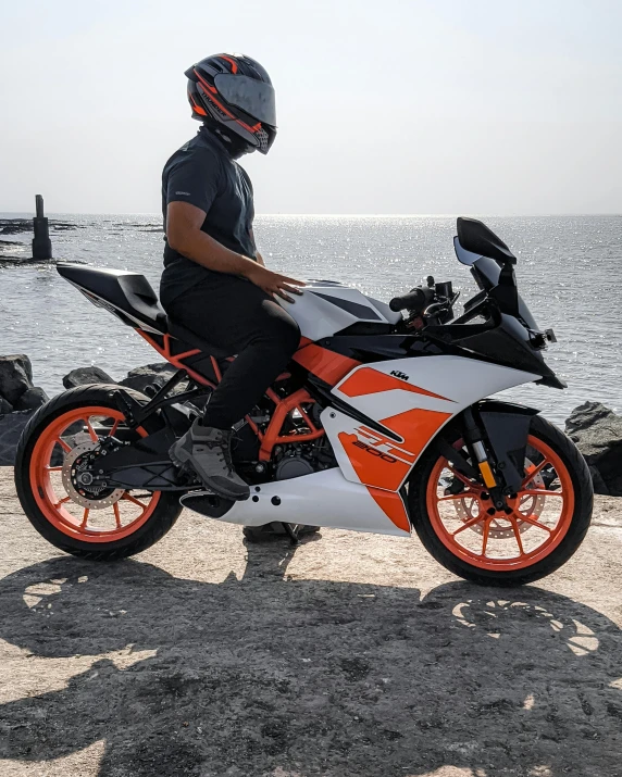 the man wearing a helmet stands beside his orange and white motorcycle