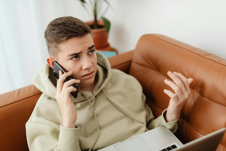 a boy sitting on the couch with his laptop talking on the phone