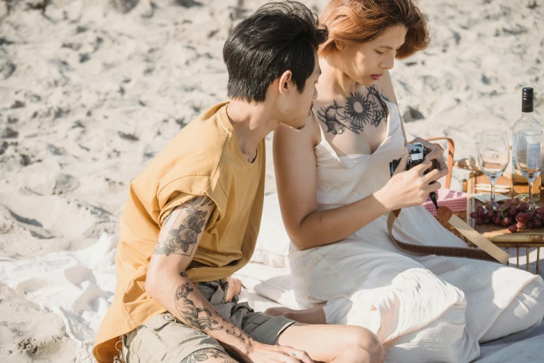 a tattooed man and woman on the beach by a picnic table