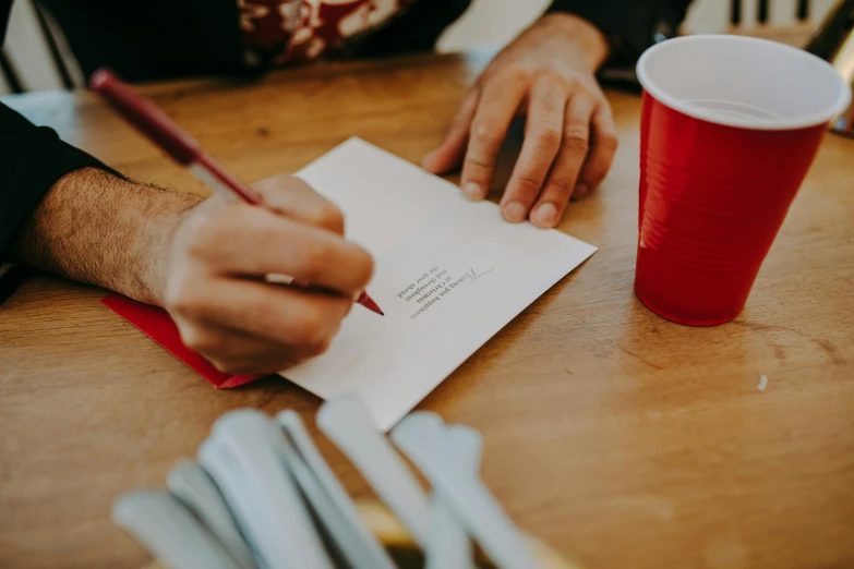 person sitting at a table writing on paper with a cup of coffee in the background