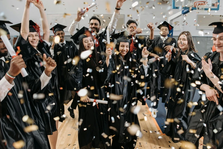 group of graduates and students with graduation caps and gowns throwing confetti on them