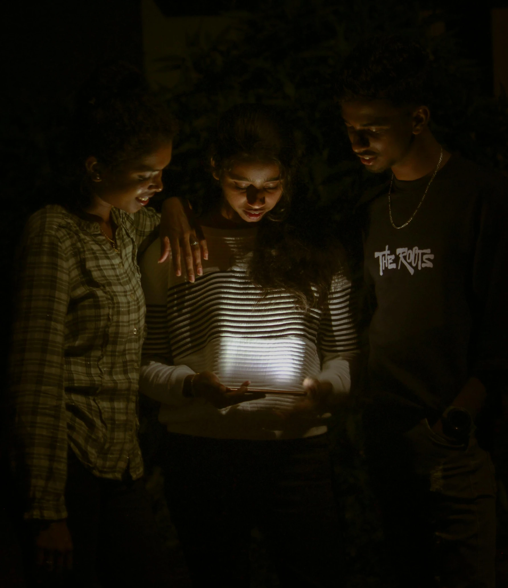 three people standing in the dark looking at a light