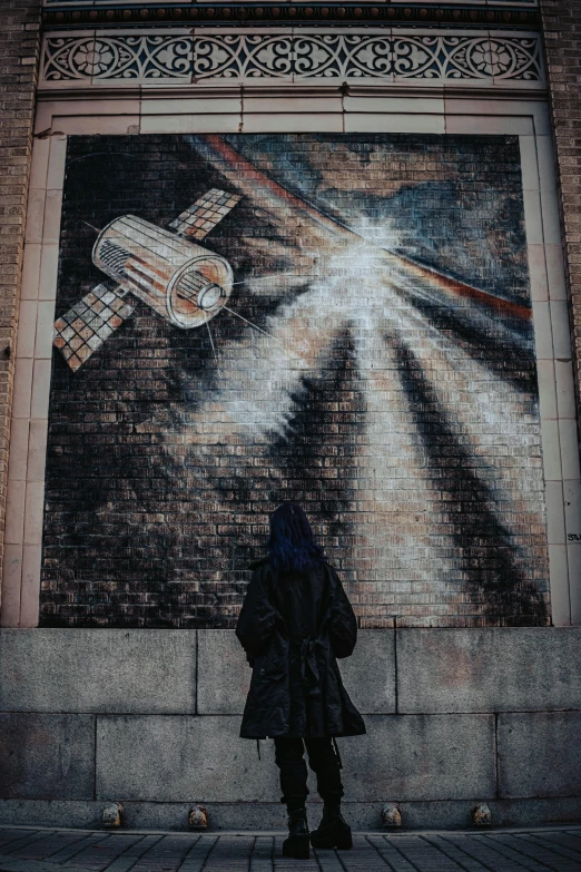 a person standing next to a mural that depicts a satellite