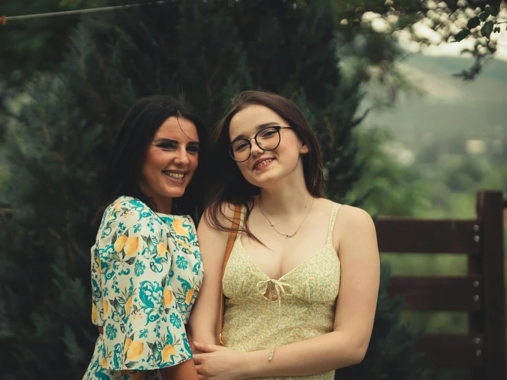 two women pose together with trees in the background