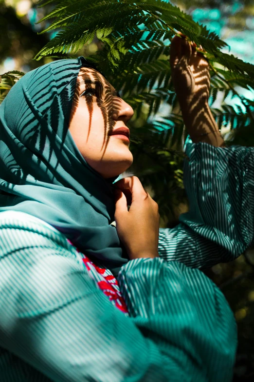 woman wearing a blue shawl stands amongst ferns