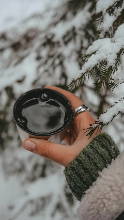 a hand holding up a coffee cup in the snow