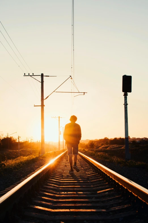 a person walking on train tracks towards the sun