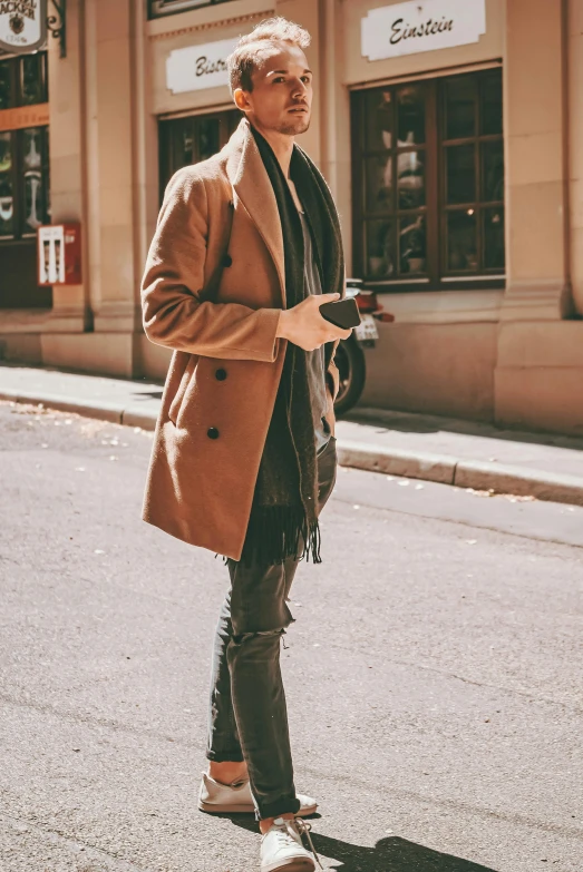 a man in brown coat holding onto his camera while standing on the street