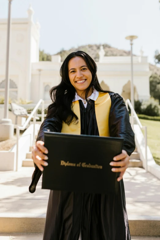 a woman in a black robe and hat smiles holding a computer screen