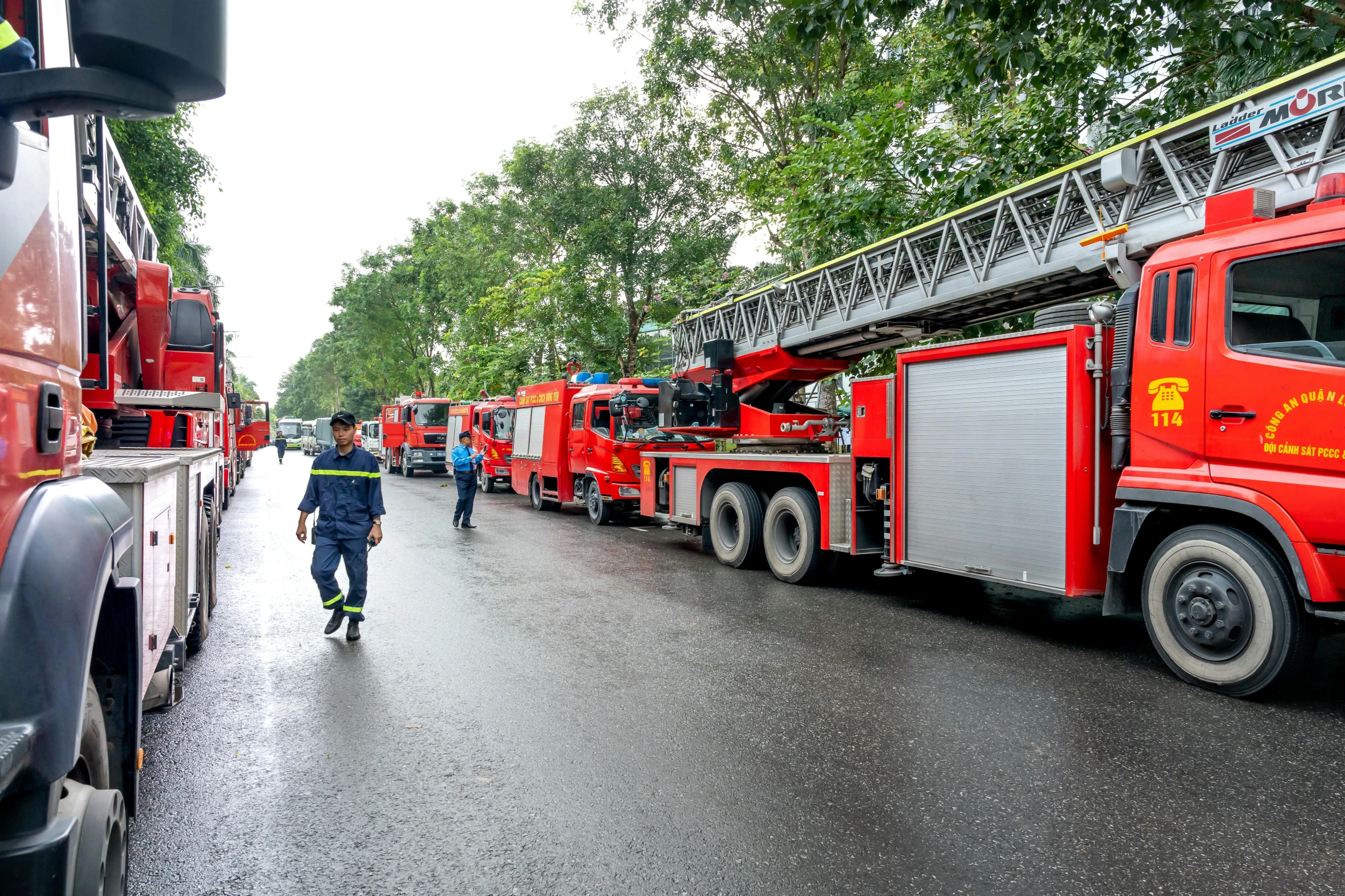 many fire trucks parked along the street with people standing on them