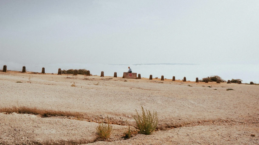 several stones, fences and poles stand on the sand near a hill