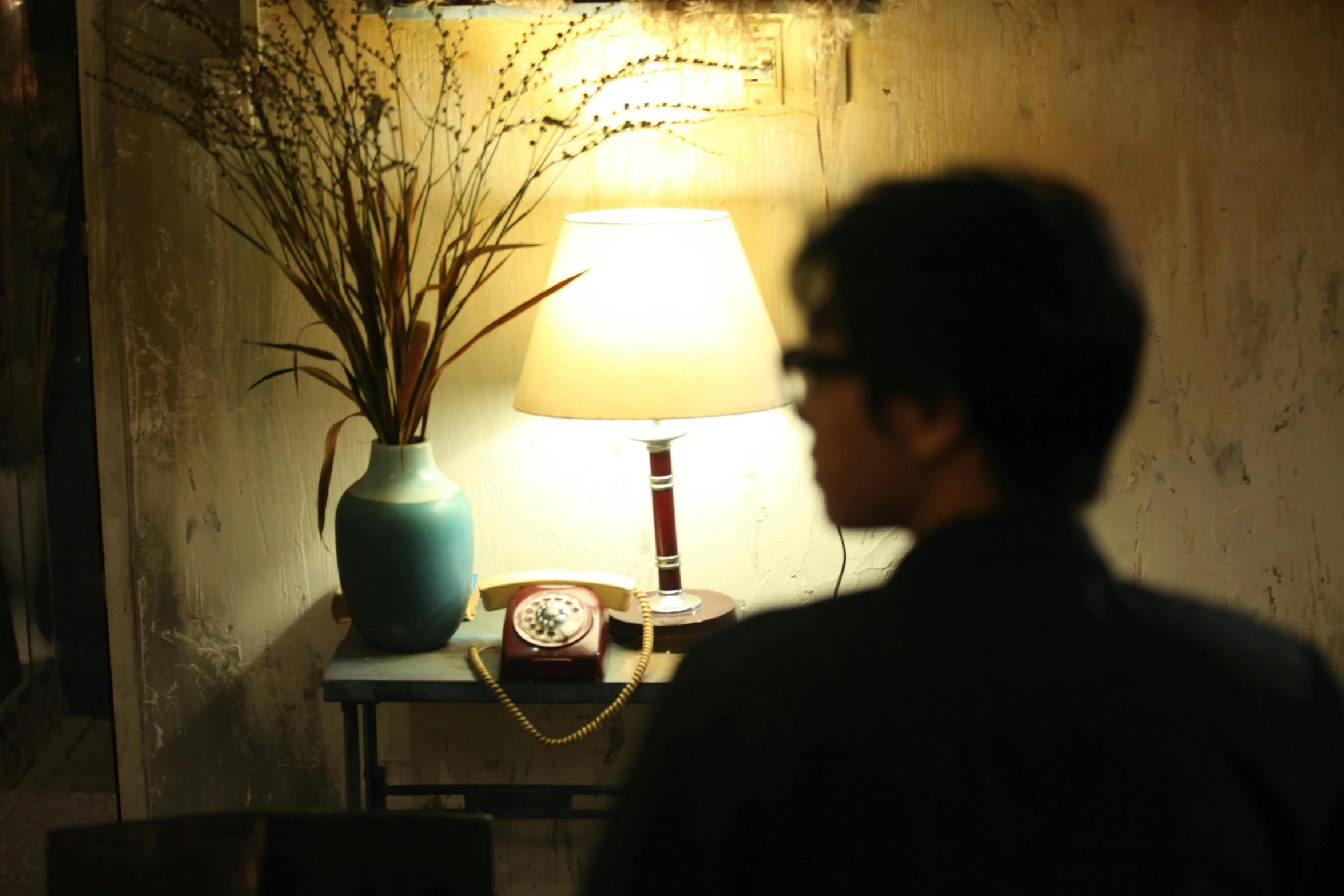 man in front of a lamp staring at clock on the side table