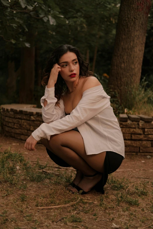 a woman crouches in the grass as she puts on her red lipstick