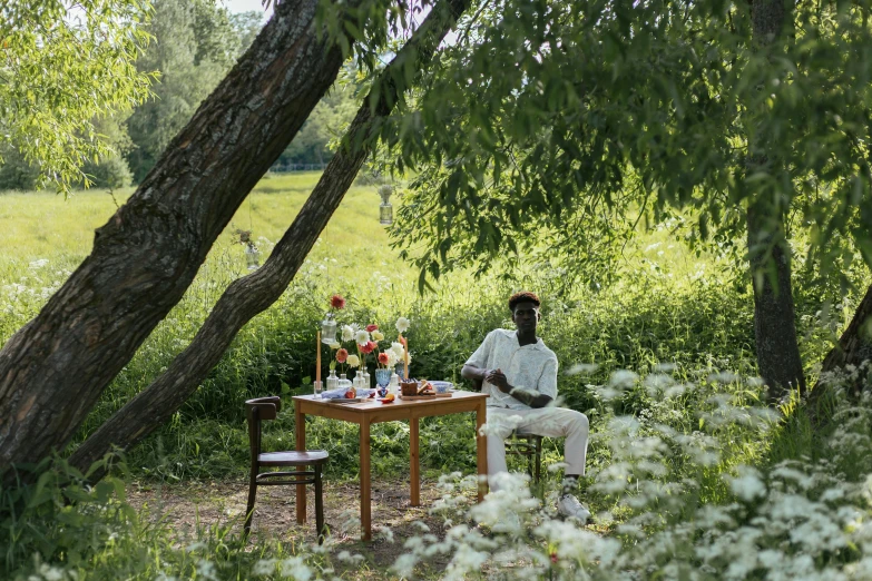 a man sits at a small table under trees