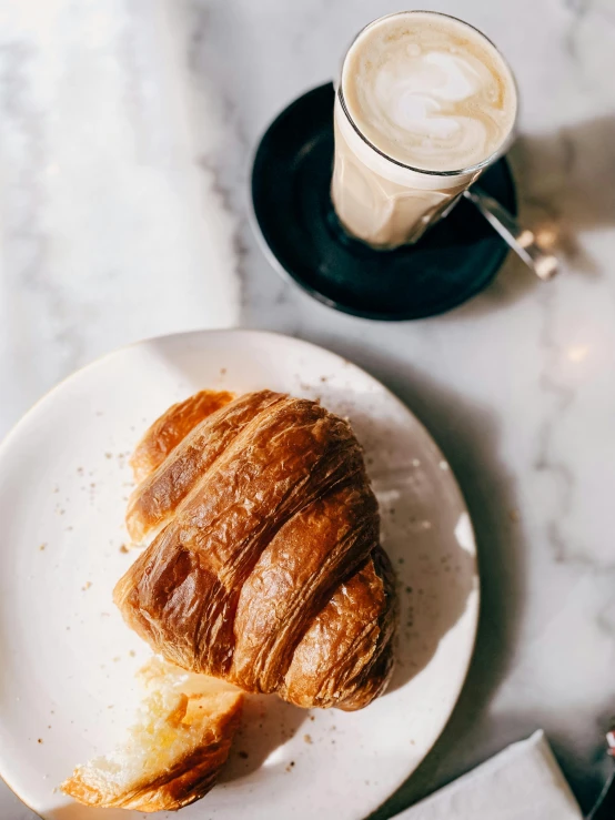 two croissants sitting on top of a plate near a glass of drink