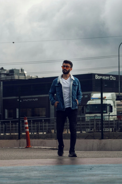 a man in a blue jacket and black jeans is standing in front of an orange cone