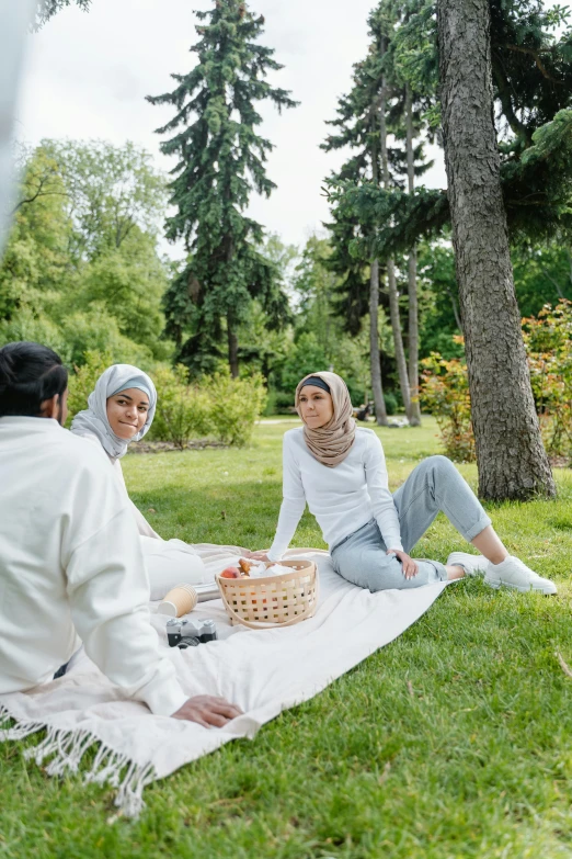 two ladies sit on a blanket and eat breakfast outside