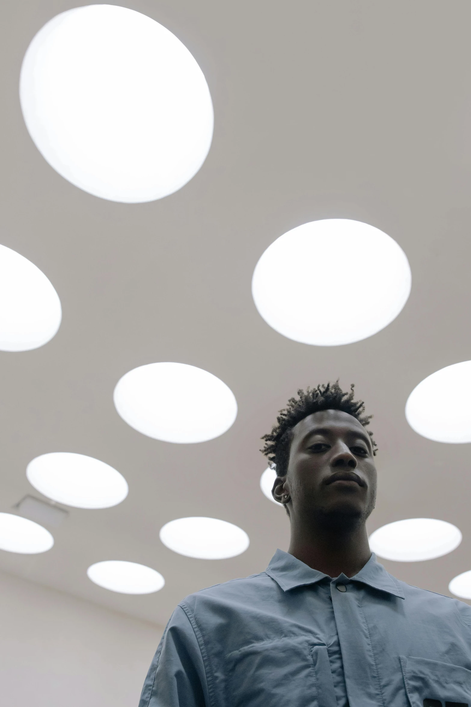 a young man looks up at the ceiling with large, circular lights