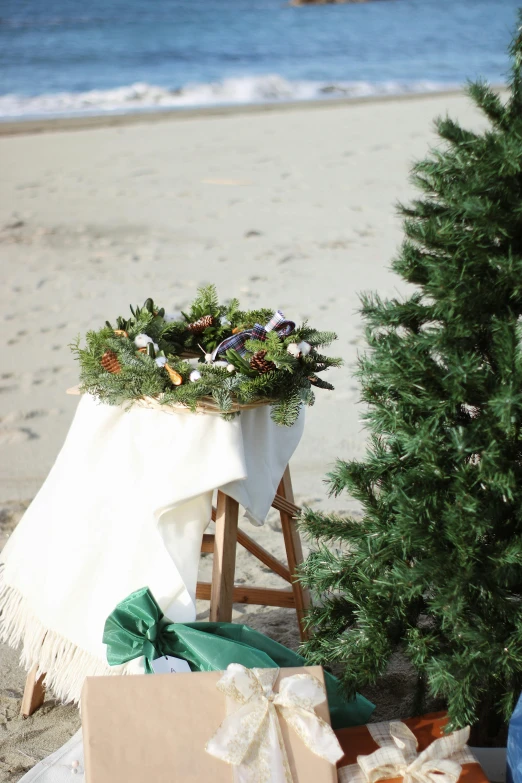 a christmas tree sits on the beach with some presents under it