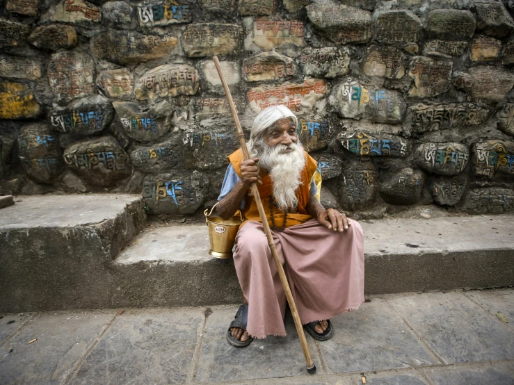 a man sitting on stairs holding a stick and pointing at soing