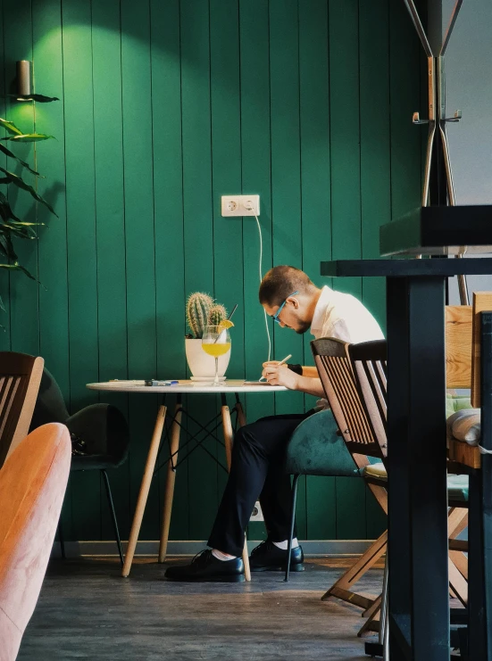 a man sitting at a table in front of a green wall