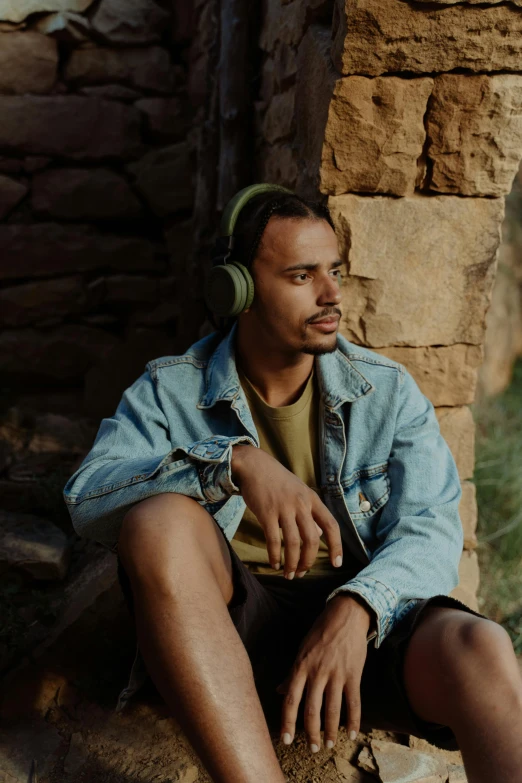 man with headphones sitting on rock beside wall