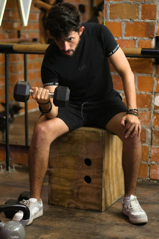 a man is holding two dumbs while sitting on a wooden box