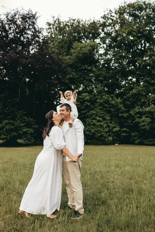 a woman in a white dress and a man hold a baby on their shoulders