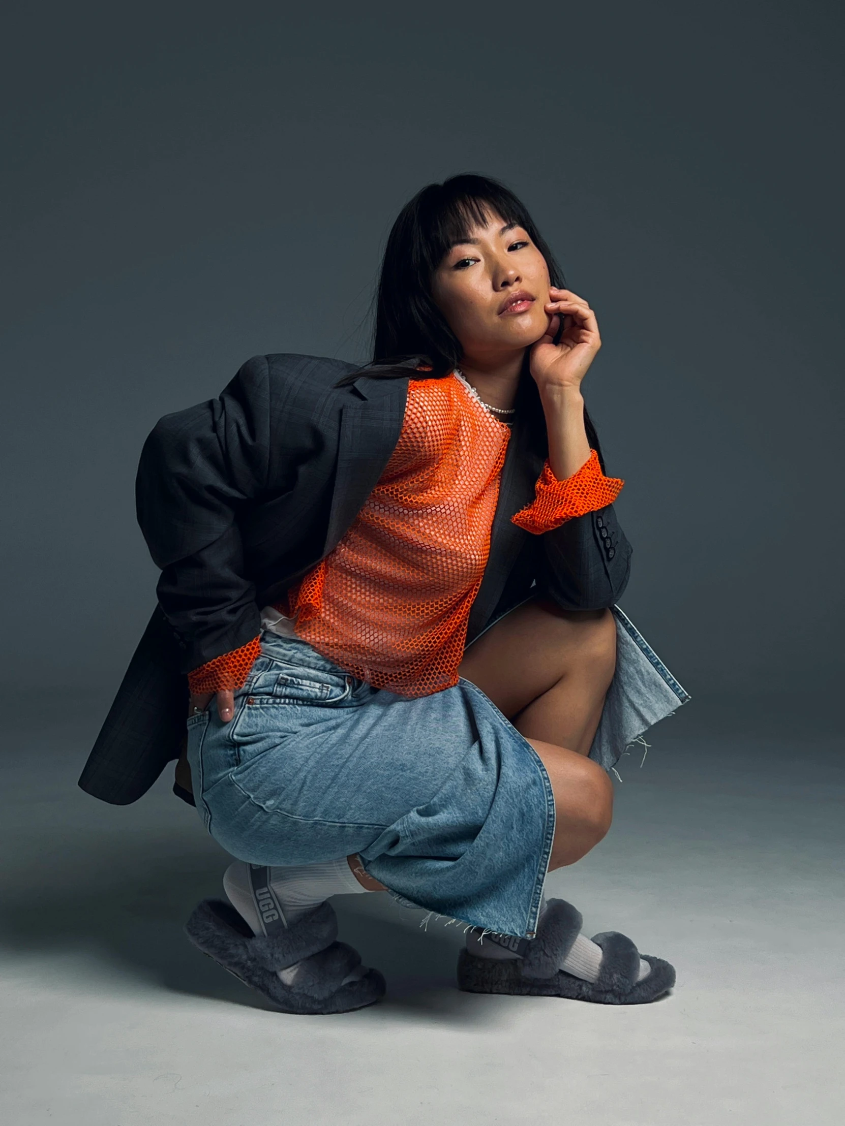 a young asian woman kneeling in jeans and an oversized jacket and scarf