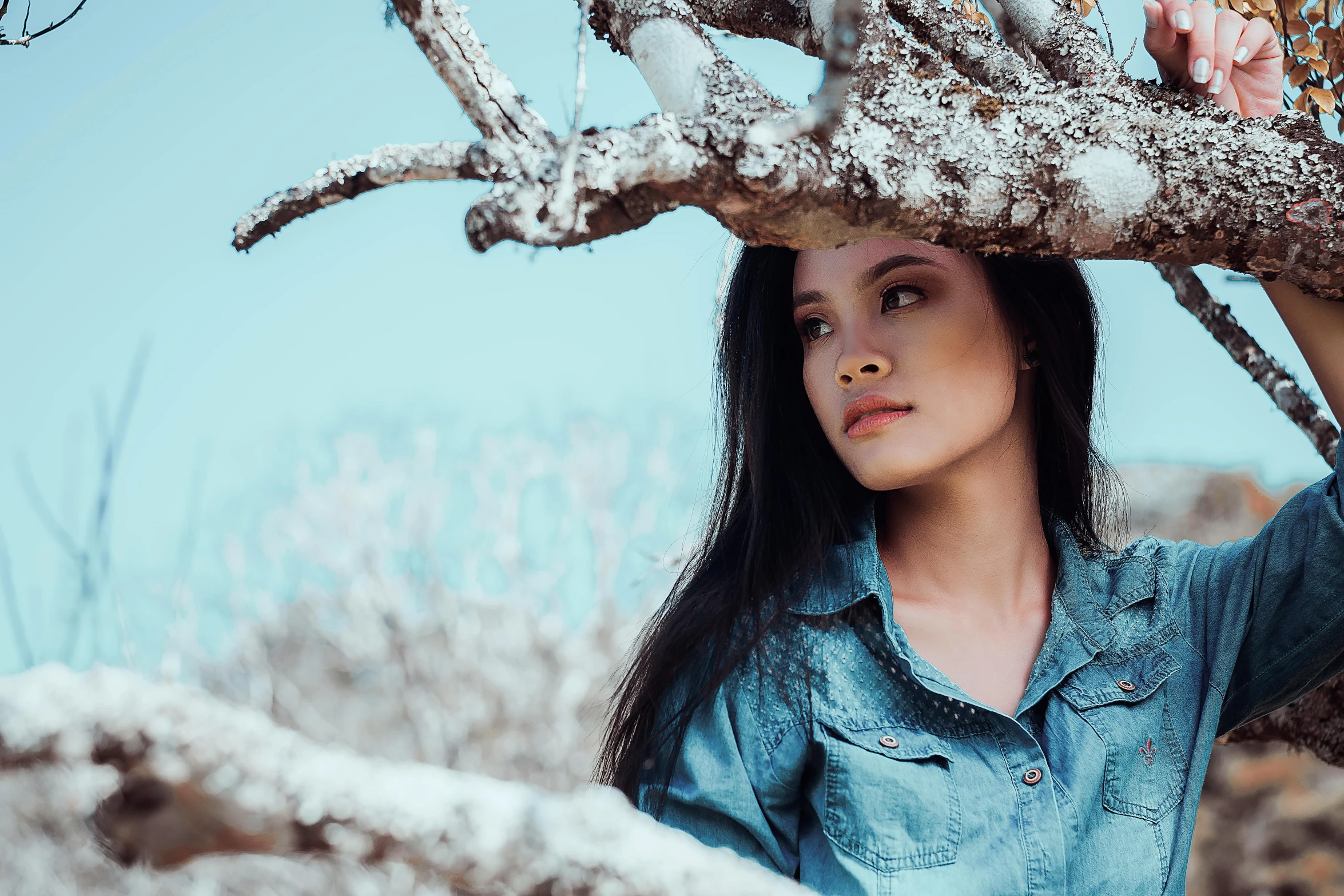 the woman is holding her head out behind a tree