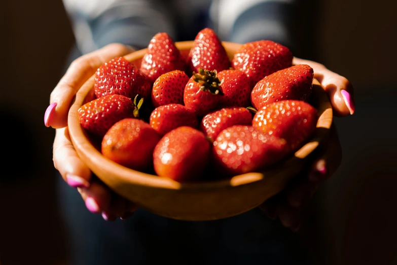 someone is holding a bowl of strawberries on a plate