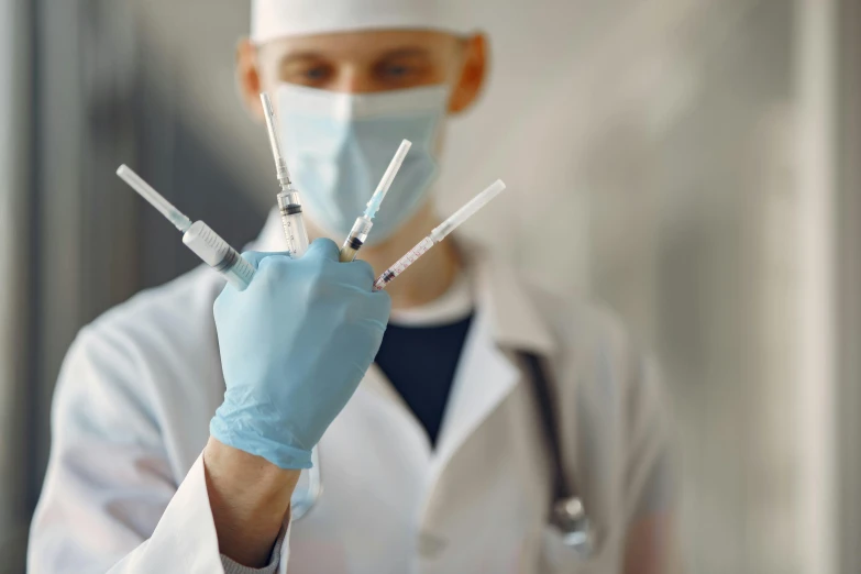 male doctor wearing blue gloves and white coat holding three sys