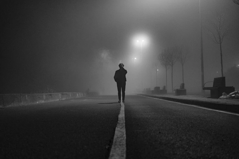 a man in black jacket walking on street next to street light