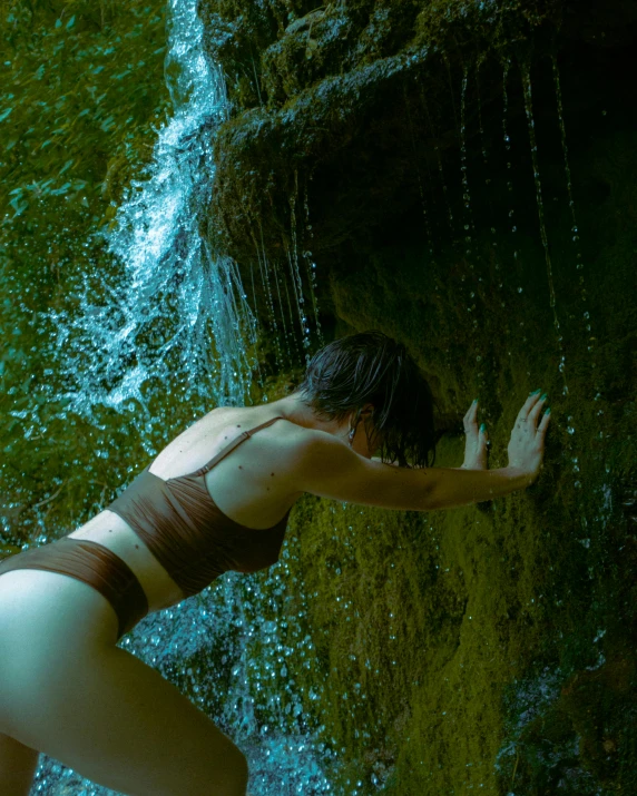 an attractive woman standing near a waterfall holding onto some water