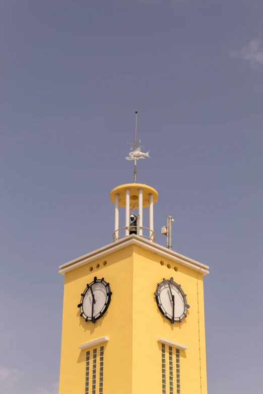 the yellow clock tower has a weather vane on the top