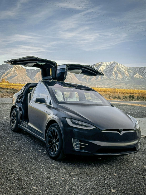 a dark colored tesla - electric car with its doors open