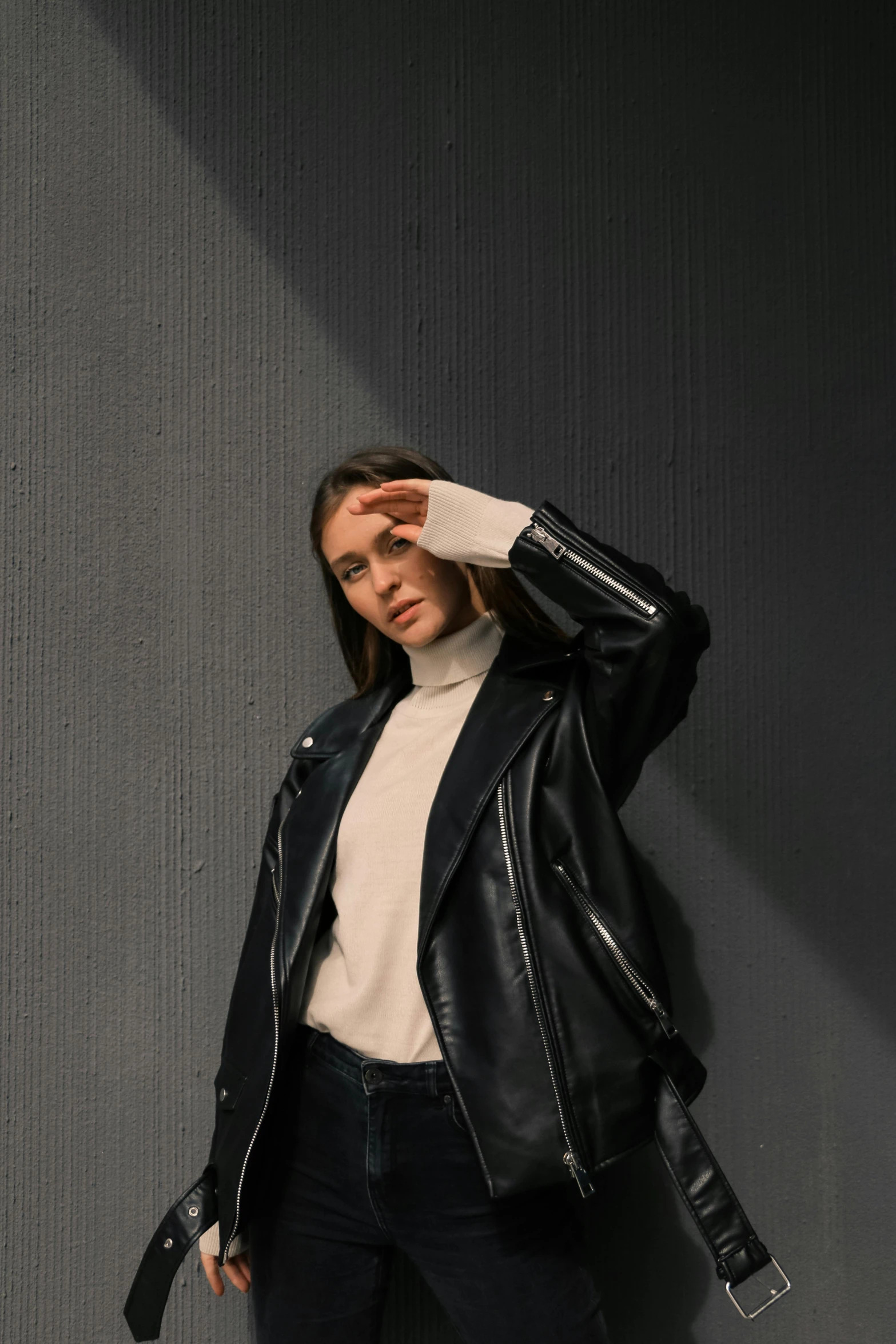 young woman wearing black leather jacket standing against grey wall