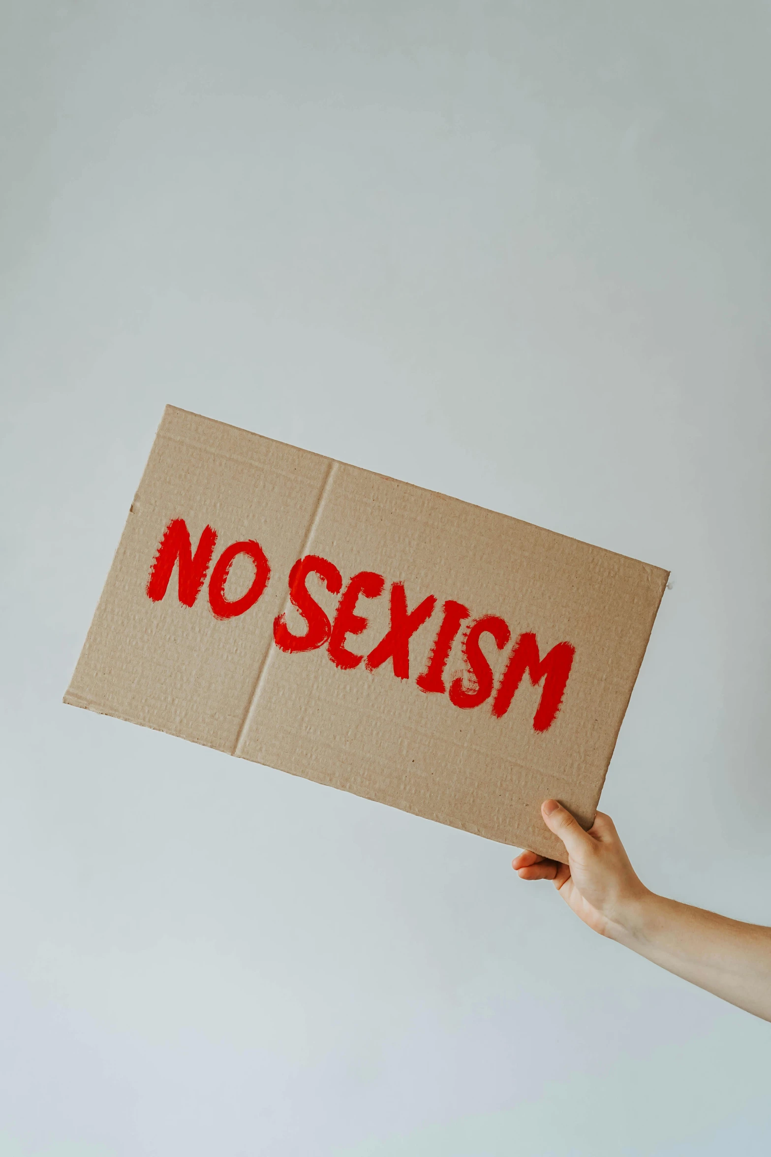 a hand holding a cardboard sign with red writing