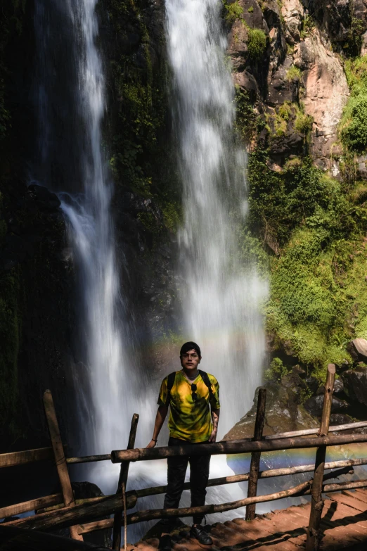 a man in a yellow shirt standing in front of a waterfall