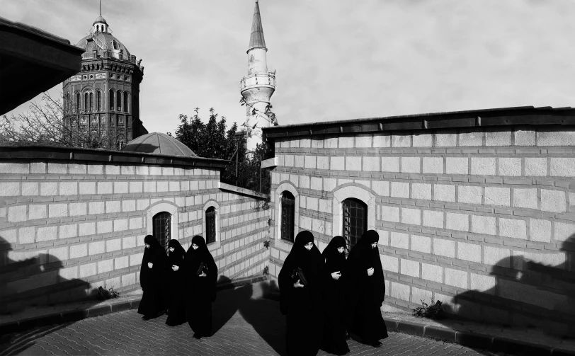 people stand in a line in a courtyard by a stone wall